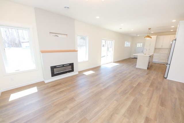 unfurnished living room featuring recessed lighting, a glass covered fireplace, light wood-style floors, a sink, and baseboards