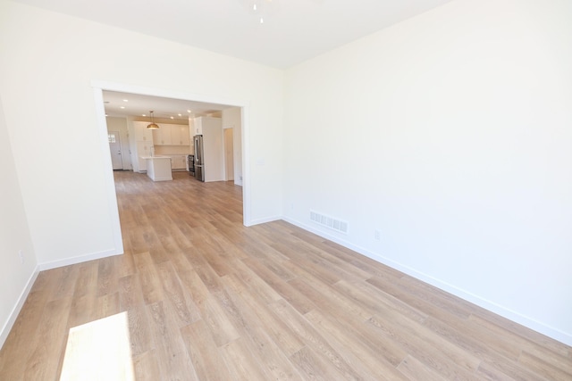 empty room with baseboards, visible vents, and light wood finished floors