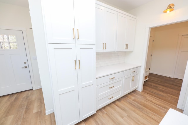 interior space featuring light wood-style floors, light countertops, white cabinetry, and backsplash