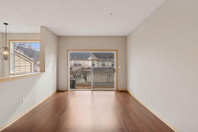 empty room with a chandelier, a textured ceiling, baseboards, and wood finished floors