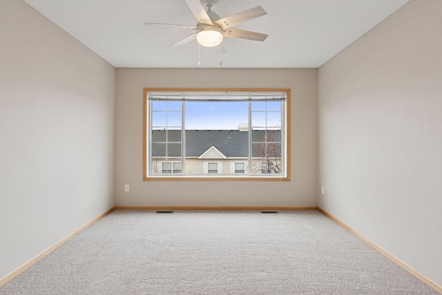 carpeted empty room featuring baseboards, visible vents, and a ceiling fan