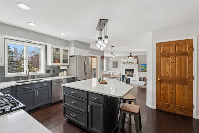 kitchen featuring dark wood-type flooring, a sink, light stone counters, a glass covered fireplace, and stainless steel appliances