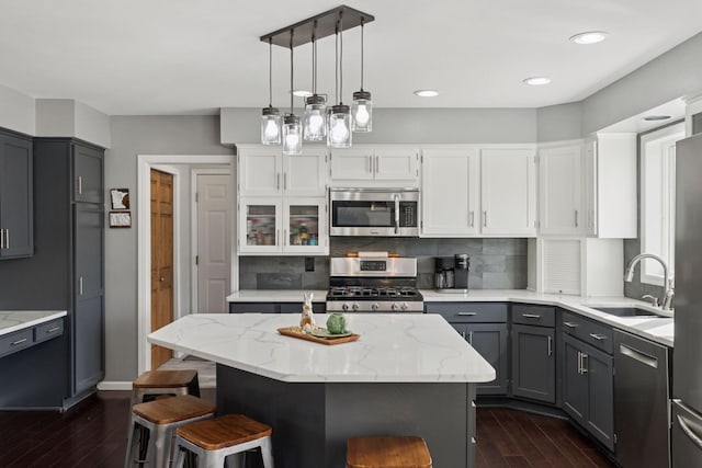 kitchen with light stone counters, dark wood finished floors, gray cabinetry, a sink, and appliances with stainless steel finishes