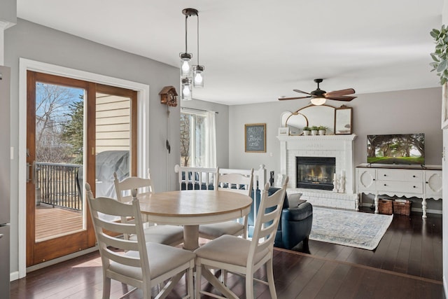 dining area with dark wood finished floors, a brick fireplace, and ceiling fan