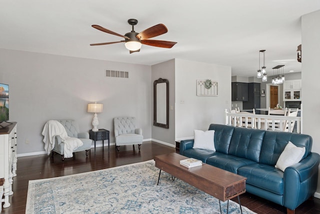 living area with dark wood-style floors, visible vents, a ceiling fan, and baseboards