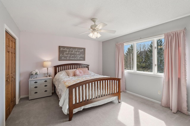 bedroom with a ceiling fan, light colored carpet, baseboards, and a textured ceiling