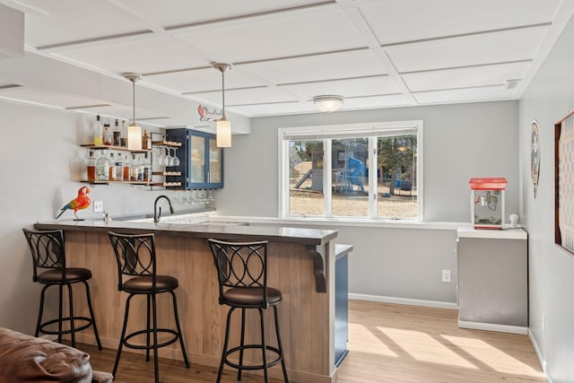 bar with baseboards, wet bar, light wood-style flooring, a sink, and pendant lighting