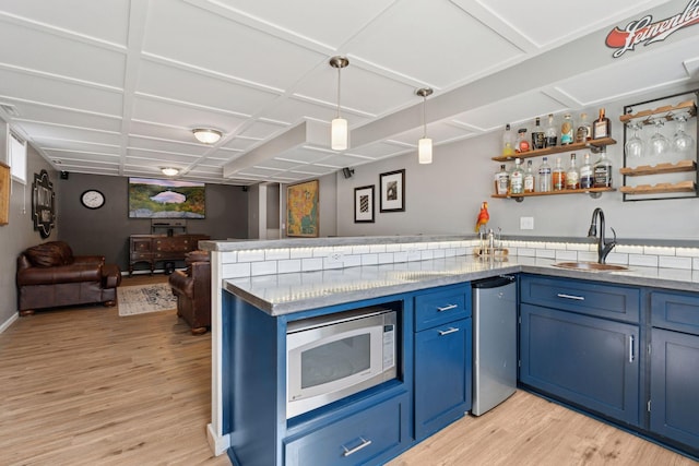 kitchen with stainless steel microwave, blue cabinetry, light wood-type flooring, a peninsula, and a sink