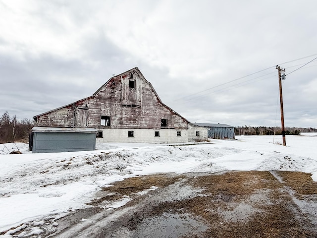 view of snow covered exterior with a garage, an outbuilding, a barn, and a gambrel roof