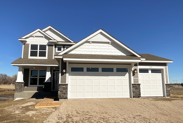 craftsman house with a garage, stone siding, driveway, and a shingled roof