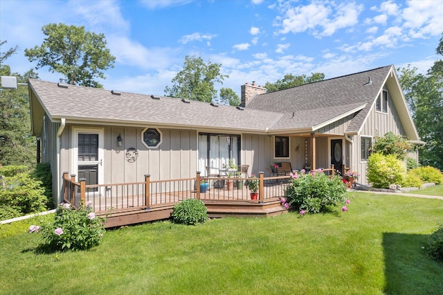 back of house featuring roof with shingles, a yard, a chimney, board and batten siding, and a deck