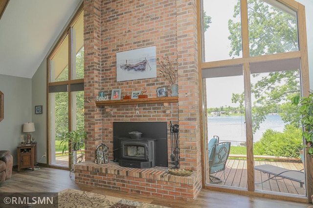 unfurnished living room featuring high vaulted ceiling, a wood stove, a water view, and wood finished floors