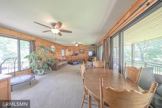 dining space with a sunroom, carpet, wooden walls, and a textured ceiling