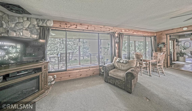 living area with a textured ceiling, a stone fireplace, carpet, and wooden walls