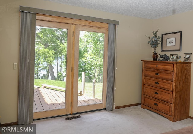 doorway with a textured ceiling, light carpet, visible vents, and a healthy amount of sunlight