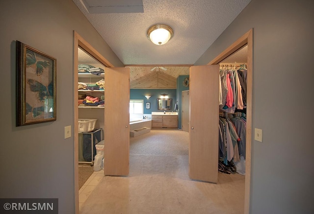 corridor featuring vaulted ceiling, a textured ceiling, and light colored carpet