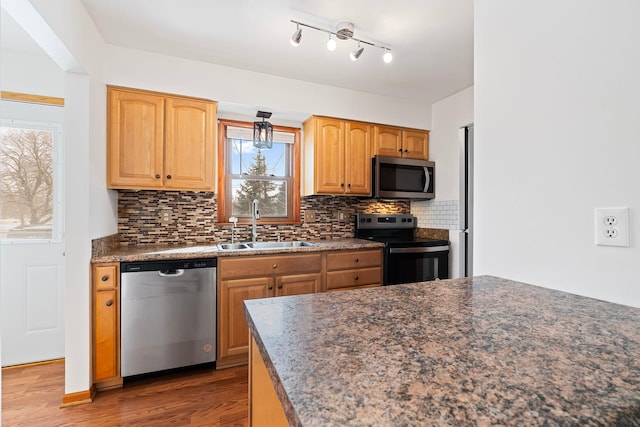 kitchen featuring dark wood-style floors, dark countertops, decorative backsplash, appliances with stainless steel finishes, and a sink