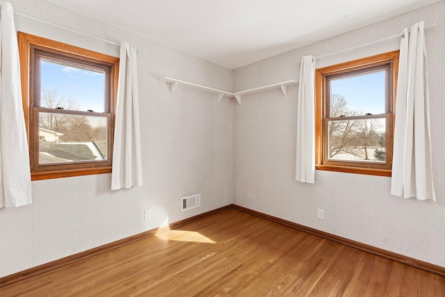 empty room with a healthy amount of sunlight, baseboards, visible vents, and wood finished floors