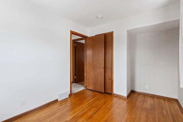 unfurnished room featuring visible vents, light wood-style flooring, baseboards, and wallpapered walls