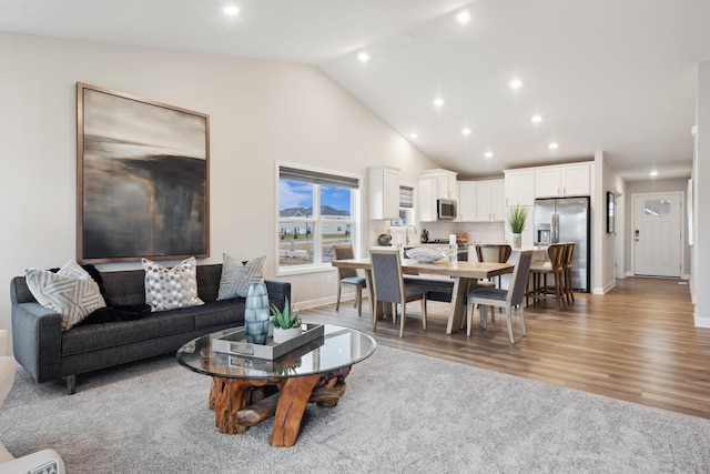 living area with baseboards, high vaulted ceiling, light wood-type flooring, and recessed lighting