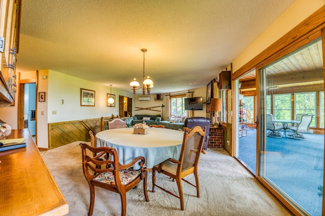 dining space featuring wooden walls, wainscoting, light colored carpet, a textured ceiling, and a chandelier