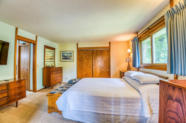 bedroom with a textured ceiling, light colored carpet, baseboards, a closet, and wallpapered walls