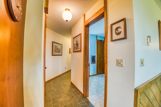 hallway featuring stone finish flooring, a textured ceiling, and baseboards