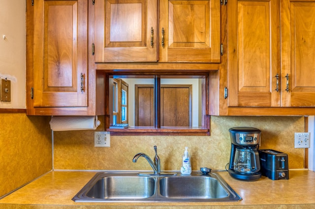 kitchen featuring light countertops, brown cabinetry, a sink, and decorative backsplash