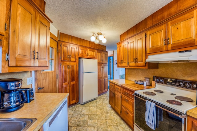 kitchen with white appliances, brown cabinets, light countertops, a textured ceiling, and under cabinet range hood