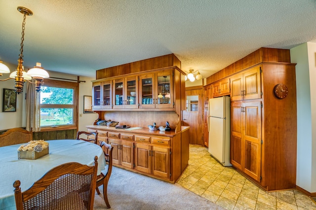 kitchen featuring decorative light fixtures, freestanding refrigerator, brown cabinetry, glass insert cabinets, and an inviting chandelier