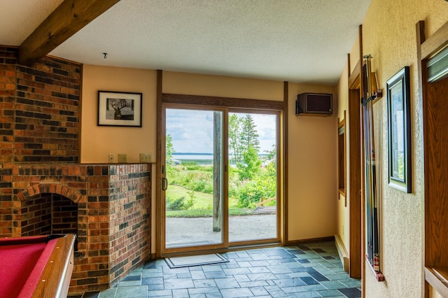 doorway to outside with baseboards, a wall unit AC, beamed ceiling, a textured ceiling, and stone tile flooring