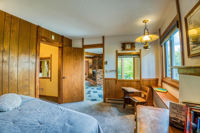 carpeted bedroom featuring wainscoting, wooden walls, baseboard heating, and a textured ceiling