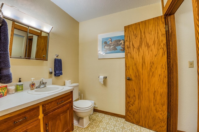 half bathroom featuring a textured ceiling, toilet, vanity, baseboards, and tile patterned floors