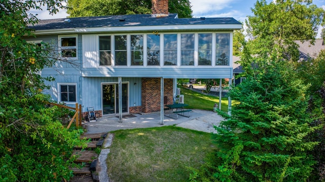 rear view of property with a patio, a lawn, a chimney, and a sunroom