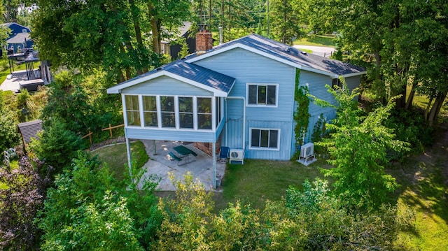 rear view of house featuring driveway, a lawn, a sunroom, a chimney, and roof with shingles