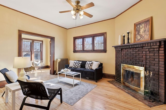 living area featuring crown molding, radiator, a brick fireplace, light wood-type flooring, and baseboards