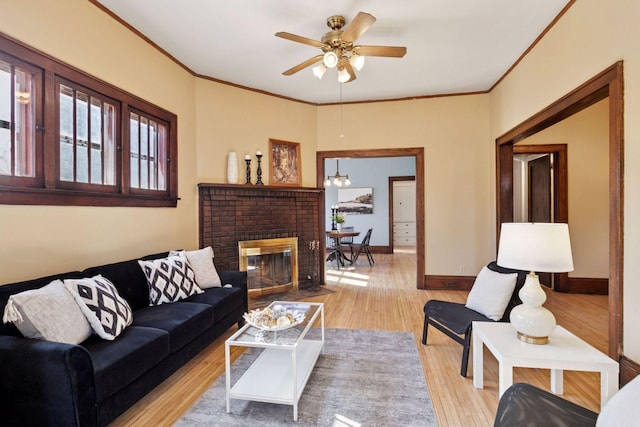 living room with ornamental molding, a ceiling fan, a brick fireplace, wood finished floors, and baseboards