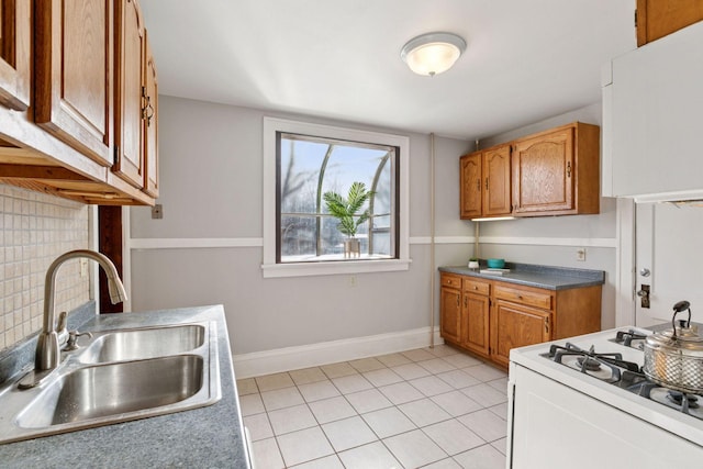 kitchen featuring gas range gas stove, light tile patterned floors, backsplash, brown cabinetry, and a sink