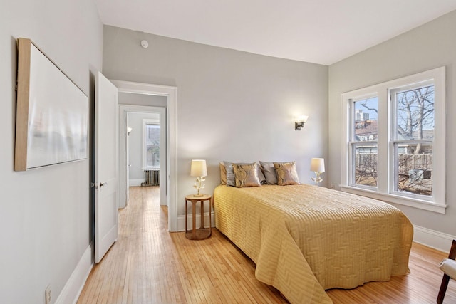 bedroom with baseboards, light wood-style flooring, and radiator