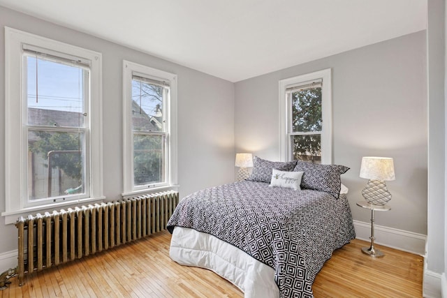 bedroom featuring hardwood / wood-style flooring, radiator heating unit, and baseboards