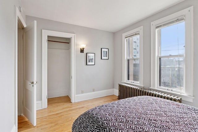 bedroom featuring baseboards, light wood-style floors, a closet, and radiator