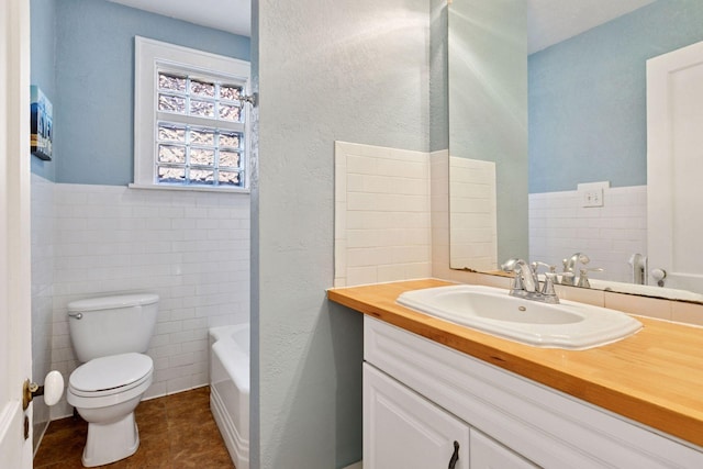 full bathroom with toilet, a wainscoted wall, vanity, tile walls, and a bathtub