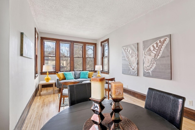 dining room featuring light wood-style floors, a textured ceiling, and baseboards