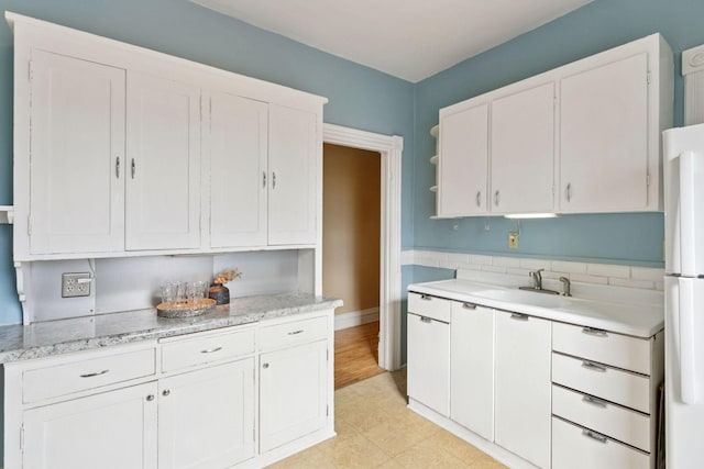 kitchen featuring freestanding refrigerator, light floors, white cabinetry, open shelves, and a sink