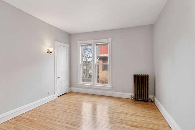 spare room featuring baseboards, light wood-type flooring, and radiator