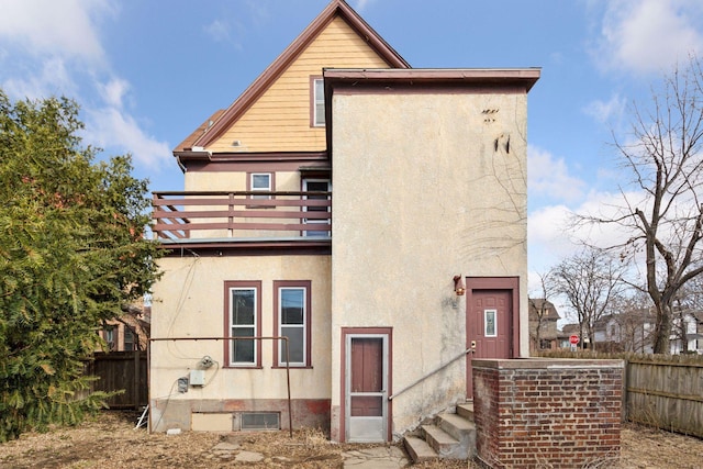 back of house with fence, a balcony, and stucco siding