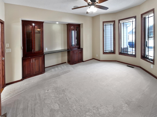 empty room with ceiling fan, a textured ceiling, light carpet, visible vents, and baseboards