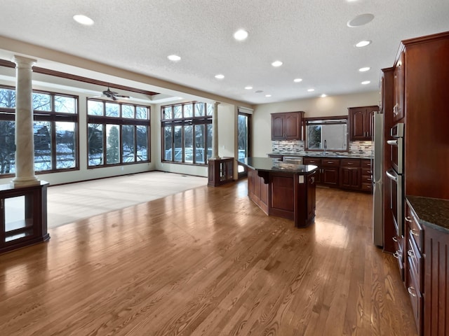 kitchen featuring decorative columns, decorative backsplash, dark wood-type flooring, a center island, and a sink