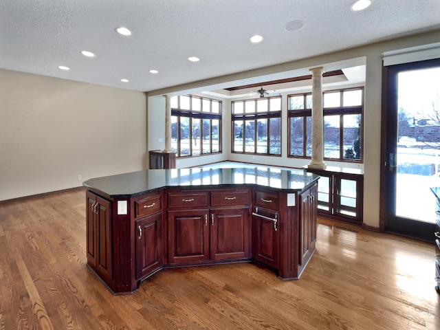 kitchen with reddish brown cabinets, dark countertops, a kitchen island, and ornate columns