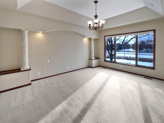 empty room with a tray ceiling, light carpet, a textured ceiling, and ornate columns